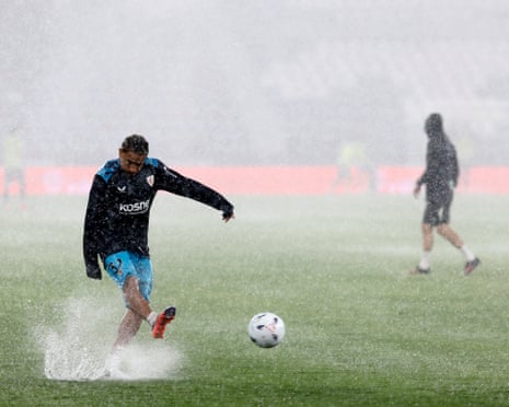 An Athletic Club soccer player kicks a ball on flooded pitch during a rainy warm-up session