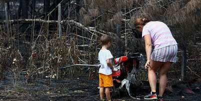 Uma mãe e seu filho inspecionam os arredores de sua casa em Le Porge, na segunda-feira, após ela ter sido destruída por um incêndio florestal Foto: Reuters / BBC News Brasil